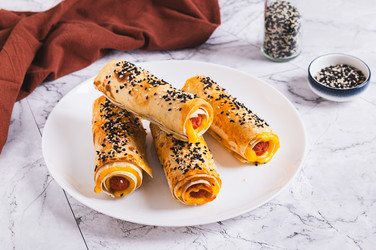 На столе на тарелке лежат поджаренные булочки с сосисками, сыром, питой и кунжутом - Elena Rui