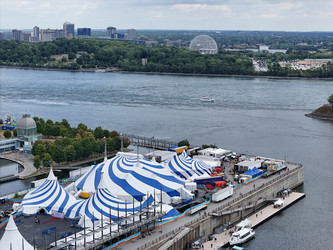 24 августа 2025 года. Полет дрона над бело-голубым шатром Cirque du Soleil в Старом порту Монреаля на фоне городского пейзажа - EOS_Canon