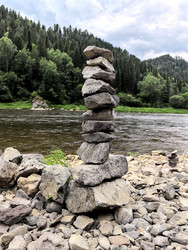 Сложенные друг на друга камни на берегу реки. На заднем плане лес и горы - Blic