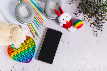 Смартфон, детские игрушки для отдыха, альбом и карандаши на столе. Вид сверху - Elena Rui