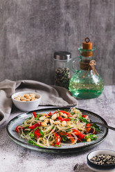 Вкусный салат из стеклянной лапши, жареного болгарского перца, кинзы и орехов на тарелке на столе (вертикальный вид) - Elena Rui