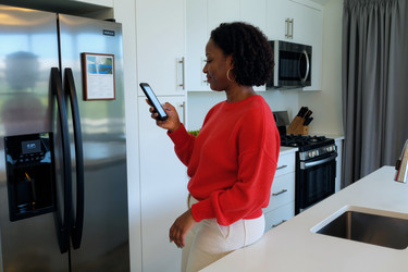 Чернокожая женщина использует смартфон на кухне для управления умным домом - AnnaStills