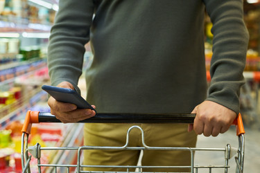 Взрослый мужчина, пользующийся смартфоном во время покупки продуктов - Pressmaster