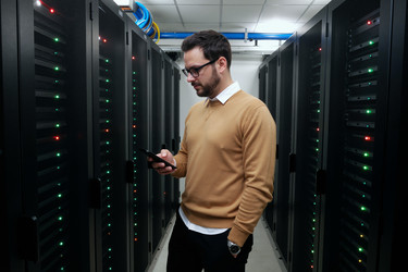 Взрослый мужчина проверяет смартфон в серверной на предмет его мониторинга - DragonImagesAsia