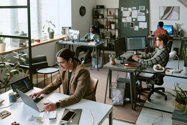 Разнообразная офисная команда, работающая за компьютерами в современном творческом рабочем пространстве - AnnaStills