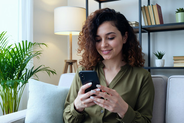 Взрослая женщина использует смартфон для обмена сообщениями в интернете дома. - AnnaStills