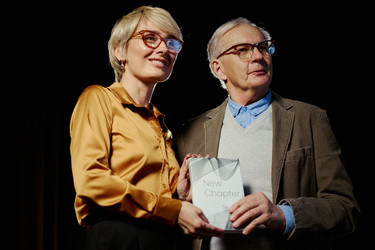Пожилой мужчина вручает книгу женщине на корпоративном мероприятии по награждению - DragonImagesAsia