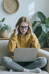 Напряженная женщина в очках испытывает головную боль во время работы за ноутбуком - DragonImagesAsia