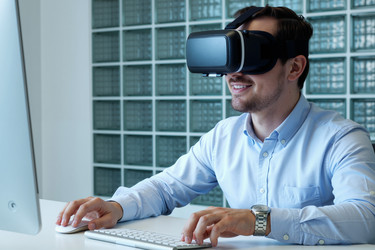Улыбающийся мужчина в Vr-гарнитуре работает за офисным столом - Pressmaster