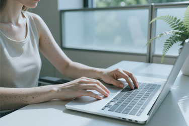 Женщина печатает на клавиатуре ноутбука, работая в современном офисе - DragonImagesAsia