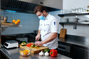 Шеф-повар в маске для лица режет овощи на коммерческой кухне - Pressmaster