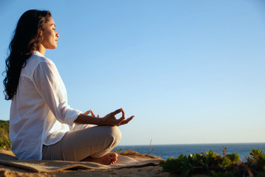 Латиноамериканская женщина медитирует в позе лотоса на утесе у океана - Pressmaster