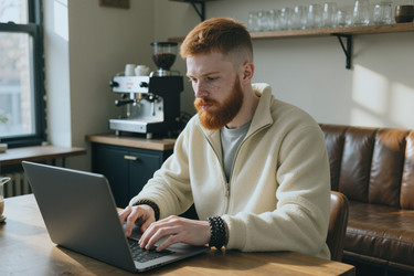 Сосредоточенный человек, работающий за ноутбуком в современном кафе или удаленном офисе - DragonImagesAsia