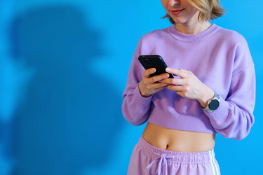 Улыбающаяся женщина, использующая смартфон для мобильного банкинга на синем фоне - DragonImagesAsia
