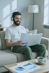 Улыбающийся мужчина в наушниках работает дома за ноутбуком - DragonImagesAsia