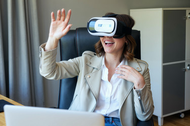 Улыбающаяся женщина в Vr-гарнитуре в офисе, имитирующая опыт работы в Метавселенной - Pressmaster