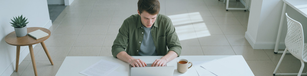 Мужчина работает за ноутбуком за письменным столом в светлом современном офисе - DragonImagesAsia