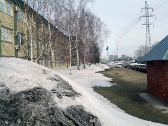 Городской пейзаж в период межсезонья с грязными снежными сугробами, промышленными трубами и линией электропередачи на заднем плане - bykgeniy