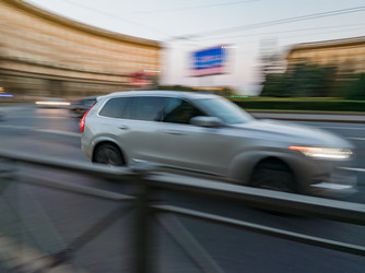 29 июля 2026 г., Россия: Серебристый кроссовер Volvo быстро едет по городской улице в сумерках. Эффект размытия движения, демонстрирующий скорость современного автомобиля - Maria Moroz