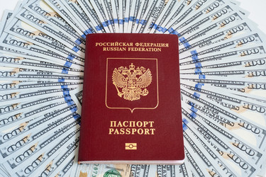 Заграничный паспорт гражданина Российской Федерации лежит на фоне купюр сто долларов США, разложенных веером - maritariny