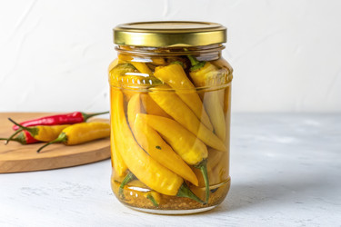 Стеклянная банка с маринованными желтыми перцами чили стоит на кухонном столе, рядом лежат еще красные перцы чили (генеративный ИИ) - RomanZ