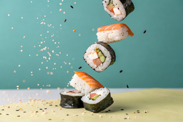 Кусочки суши, падающие на однотонный фон с разбросанными семенами кунжута. Генеративный ИИ - RomanZ