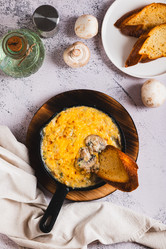 Грибы, нарезанные соломкой, со сливками и сырной корочкой, жарятся на сковороде на столешнице (вид сверху) - Elena Rui