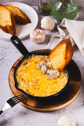 Грибы, нарезанные соломкой, со сливками и сырной корочкой, жарятся на сковороде на столе (вид сверху) - Elena Rui