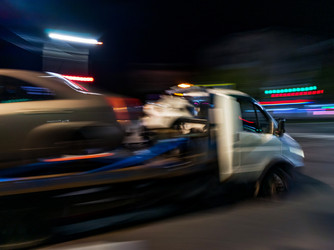 Эвакуатор, перевозящий сломанный автомобиль по городской дороге ночью. Служба помощи на дороге в движении с эффектом размытия изображения. Концепция транспортной отрасли и аварийно-спасательных работ в автомобильной сфере - Maria Moroz