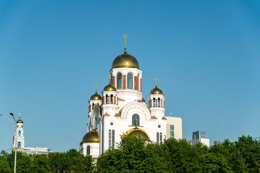 Екатеринбург, Россия. Храм на Крови в честь Всех Святых, пять позолоченных куполов-луковиц на восьмиугольных барабанах возвышаются над линией деревьев под ясным голубым небом - NikitaMaykov