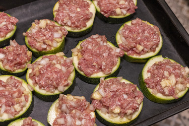 Крупный план сырых фаршированных кружочков цуккини с мясным фаршем на противне - Pazemin