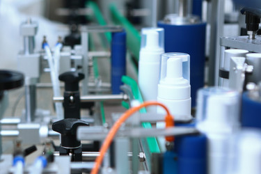 Белая пластиковая бутылка движется по конвейерной ленте. Машина для укупорки и маркировки. Производство косметики и средств по уходу за кожей. Белая пластиковая бутылка с дозатором-помпой на автоматической конвейерной линии для производства косметики - RusAKphoto