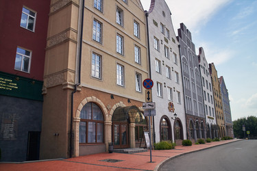 Современные здания в европейском стиле в центре Рязани, Россия. Красочные фасады с балконами, цветочными клумбами, арками и часовой башней под голубым летним небом - Irrin0215