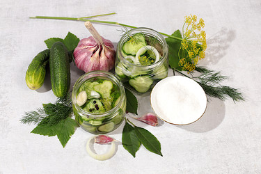 Огурцы с укропом, чесноком, хреном, листьями для засолки и маринованные огурцы в банках на кухонном столе. Концепция урожая. Рецепт и ингредиенты для домашних солений. Концепция домашнего консервирования - svetlanabalyn