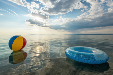 Красочный пляжный мяч и плавающий объект в спокойной воде на закате. Генеративный ИИ - RomanZ