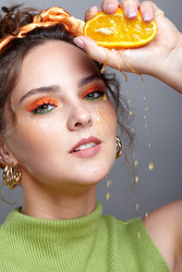 Зortrait of a young woman squeezes orange juice onto her face. Female with bright make-up on face - Serg Zastavkin