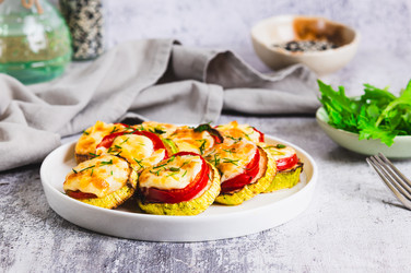 Ломтики цукини, запеченные с помидорами, сыром и чесноком на тарелке, подаются на стол - Elena Rui