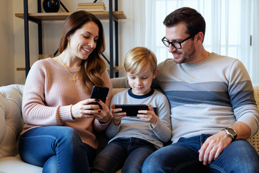 Счастливые родители наблюдают, как сын играет дома в игру на смартфоне - DragonImagesAsia