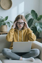 Напряженная женщина массирует виски во время работы за ноутбуком - DragonImagesAsia