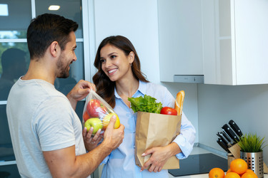 Счастливая пара распаковывает свежие продукты на кухне после похода по магазинам - Pressmaster