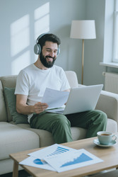 Улыбающийся мужчина в наушниках работает дома за ноутбуком - DragonImagesAsia
