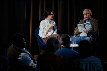 Пожилой мужчина читает книгу во время беседы автора с женщиной-модератором - DragonImagesAsia