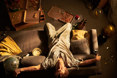 Портрет мужчины, лежащего вверх ногами на диване после домашней вечеринки - Pressmaster
