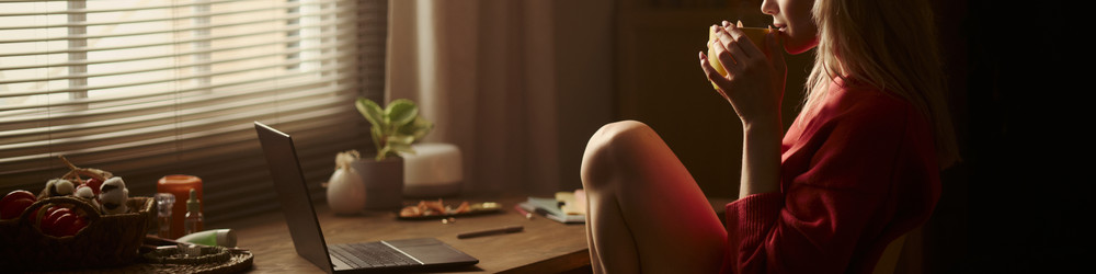 Женщина пьет кофе за столом с ноутбуком во время удаленной работы - DragonImagesAsia