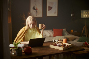 Женщина работает за ноутбуком и пьет кофе в уютном домашнем офисе - DragonImagesAsia