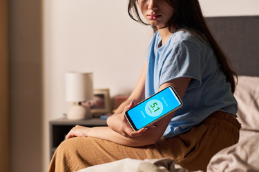 Девушка сканирует датчик глюкозы с помощью смартфона в спальне - Pressmaster