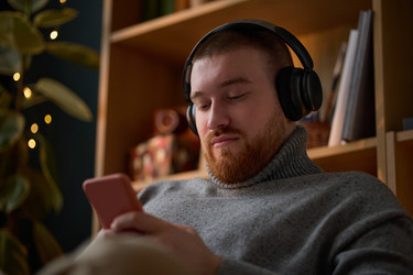 Мужчина в наушниках использует смартфон для электронного обучения дома - DragonImagesAsia
