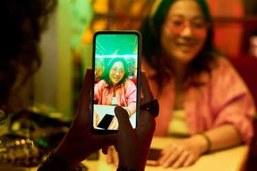 Азиатка фотографирует подругу на смартфон в кафе - Mediaphotos