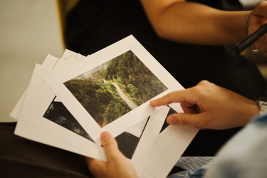 Руки мужчины, держащие и указывающие на напечатанные пейзажные фотографии - DragonImagesAsia