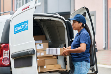 Женщина-курьер латиноамериканского происхождения загружает картонные коробки в фургон доставки - Pressmaster